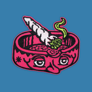 Embroidered 3.25" Ashtray Head patch with pink bowl, white joint, and green smoke on a blue background.